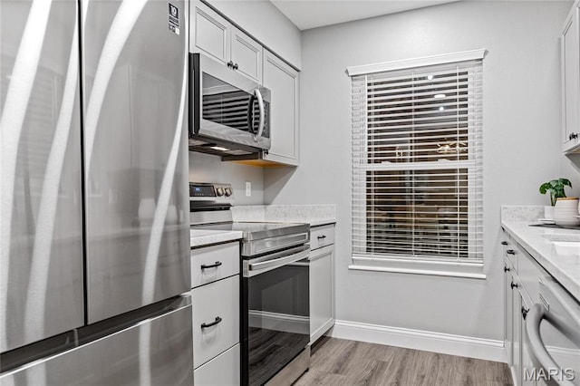 5425 Independence Rd, Weldon Spring, MO 63304 - kitchen with stainless steel appliances, light wood finished floors, white cabinets, baseboards, and light stone counters
