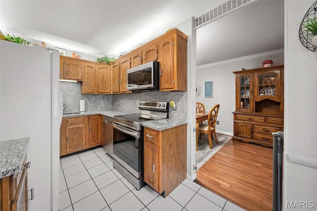 1615 Rosewall Dr Unit C, Saint Charles, MO 63303 - kitchen with appliances with stainless steel finishes, decorative backsplash, brown cabinets, light tile patterned floors, and ornamental molding