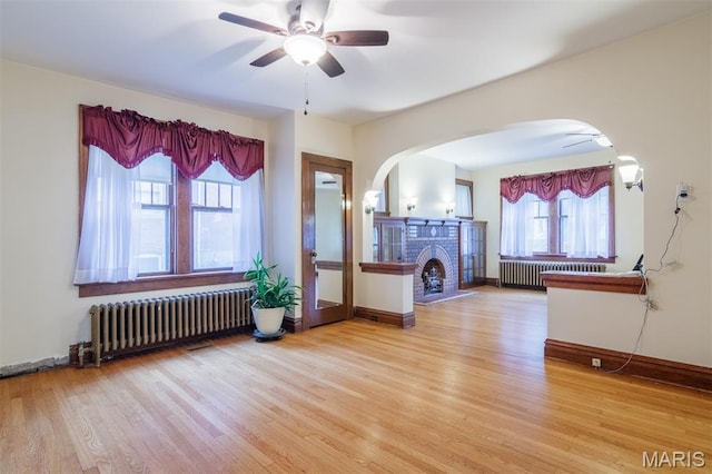 607 9th St, Highland, IL 62249 - living area featuring radiator, arched walkways, ceiling fan, light wood-style flooring, and a brick fireplace