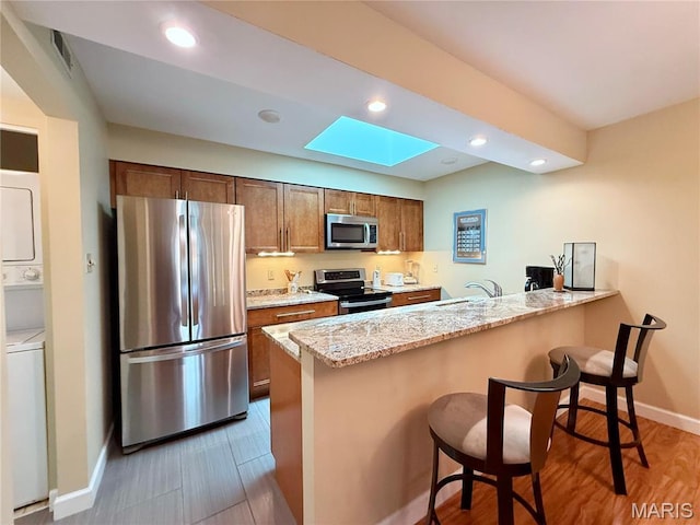 4235 W Pine Blvd Unit 21, Saint Louis, MO 63108 - kitchen with appliances with stainless steel finishes, stacked washer / dryer, a peninsula, a kitchen bar, and a sink