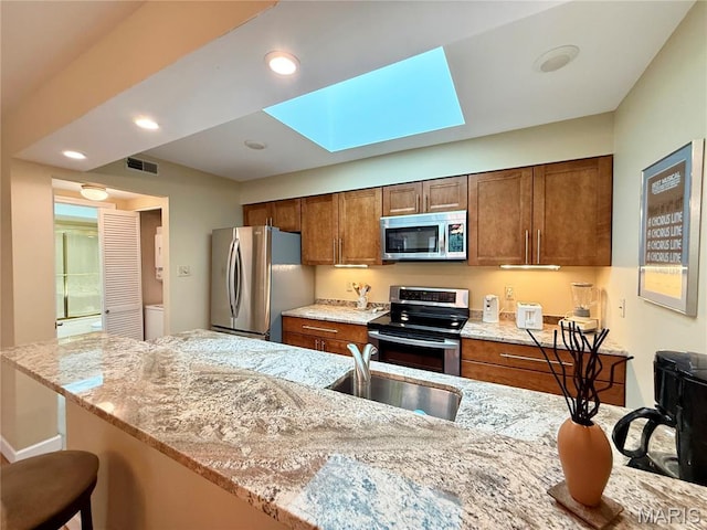 4235 W Pine Blvd Unit 21, Saint Louis, MO 63108 - kitchen with appliances with stainless steel finishes, a sink, a breakfast bar area, brown cabinetry, and light stone countertops