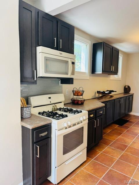 1928 Arsenal St, Saint Louis, MO 63118 - kitchen with white appliances, light tile patterned floors, decorative backsplash, light countertops, and dark cabinets