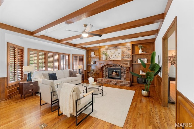 16427 Andraes Dr, Chesterfield, MO 63005 - living room featuring a wainscoted wall, beam ceiling, light wood-style flooring, ceiling fan, and a brick fireplace