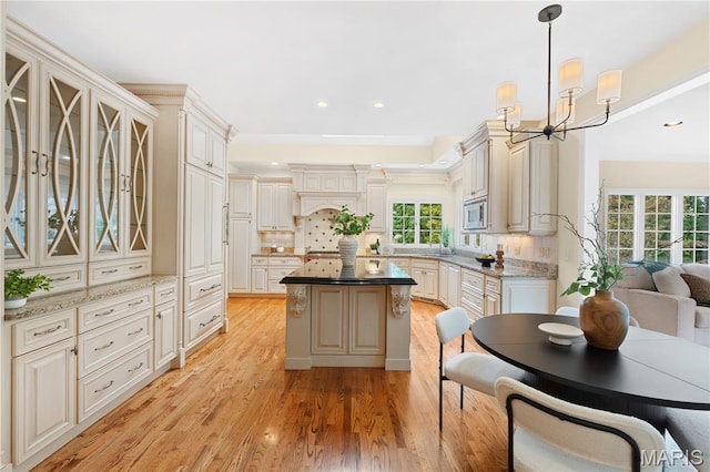16427 Andraes Dr, Chesterfield, MO 63005 - kitchen featuring stainless steel microwave, light wood-type flooring, glass insert cabinets, backsplash, and a kitchen island