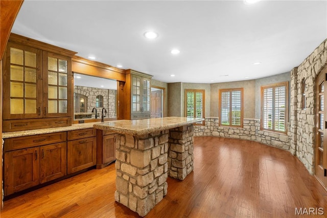 16427 Andraes Dr, Chesterfield, MO 63005 - kitchen with brown cabinetry, light wood-type flooring, glass insert cabinets, light stone counters, and a center island