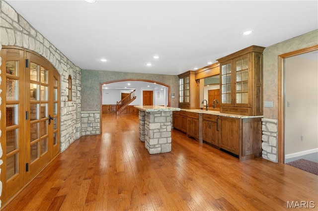 16427 Andraes Dr, Chesterfield, MO 63005 - kitchen with brown cabinetry, arched walkways, light wood-style floors, glass insert cabinets, and recessed lighting