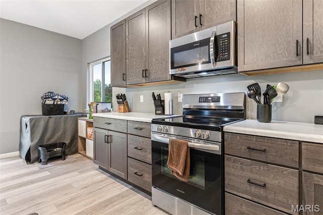 kitchen with stainless steel appliances, light wood-type flooring, light countertops, and dark brown cabinetry