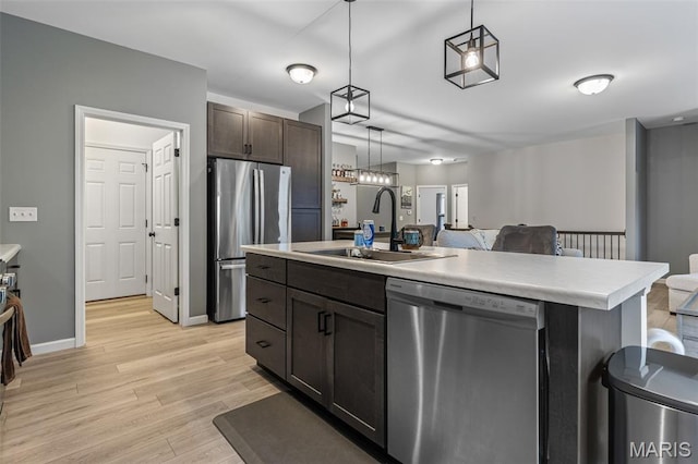 kitchen with stainless steel appliances, a sink, light countertops, dark brown cabinetry, and light wood-type flooring