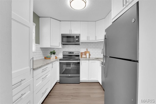 9179 N Swan Cir, Brentwood, MO 63144 - kitchen with appliances with stainless steel finishes, a textured ceiling, white cabinets, light wood-style floors, and tasteful backsplash