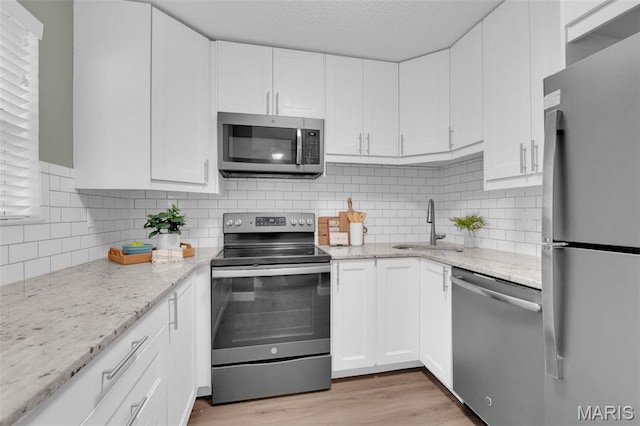 9179 N Swan Cir, Brentwood, MO 63144 - kitchen with appliances with stainless steel finishes, a sink, white cabinets, light wood-type flooring, and a textured ceiling