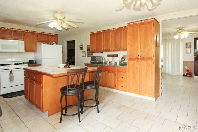 17748 State Highway C, Advance, MO 63730 - kitchen with white appliances, a ceiling fan, tile counters, a center island, and a kitchen bar