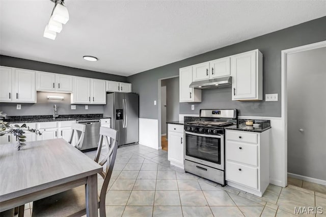 12006 Glengrove Dr, Maryland Heights, MO 63043 - kitchen featuring appliances with stainless steel finishes, under cabinet range hood, white cabinetry, dark countertops, and light tile patterned floors