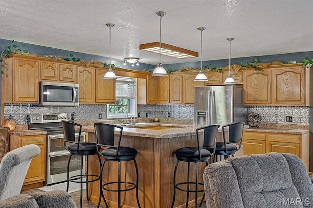 17504 Division St, Kennett, MO 63857 - kitchen featuring stainless steel appliances, a kitchen island, a kitchen bar, a textured ceiling, and backsplash
