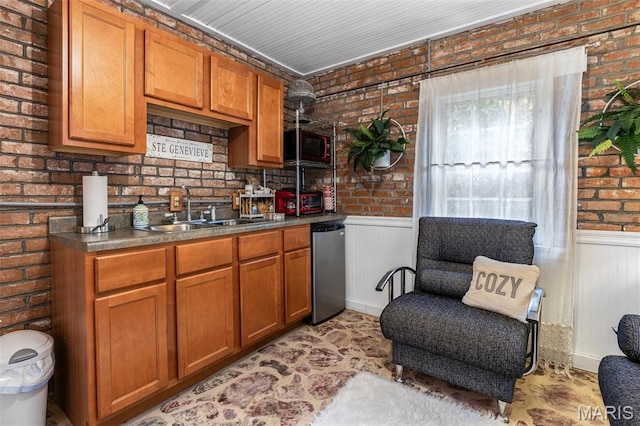 698N 3rd St, Saint Genevieve, MO 63670 - kitchen featuring brick wall, brown cabinetry, a wainscoted wall, and dark countertops