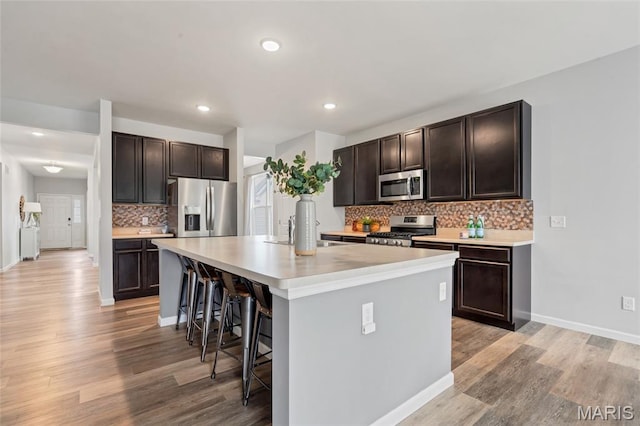 803 Brimley Dr, Cottleville, MO 63304 - kitchen featuring stainless steel appliances, light wood-type flooring, a breakfast bar area, an island with sink, and dark brown cabinets