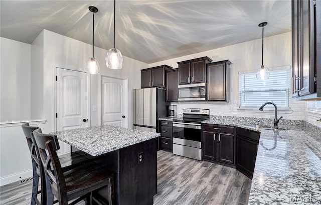 1810 Barclay Bluff Ct, Wentzville, MO 63385 - kitchen featuring appliances with stainless steel finishes, wood finished floors, a center island, light stone counters, and a kitchen bar