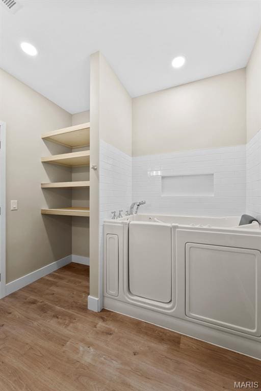 63 Plackemeier Dr, Ofallon, MO 63366 - bathroom featuring a garden tub, wood finished floors, recessed lighting, washing machine and dryer, and wainscoting