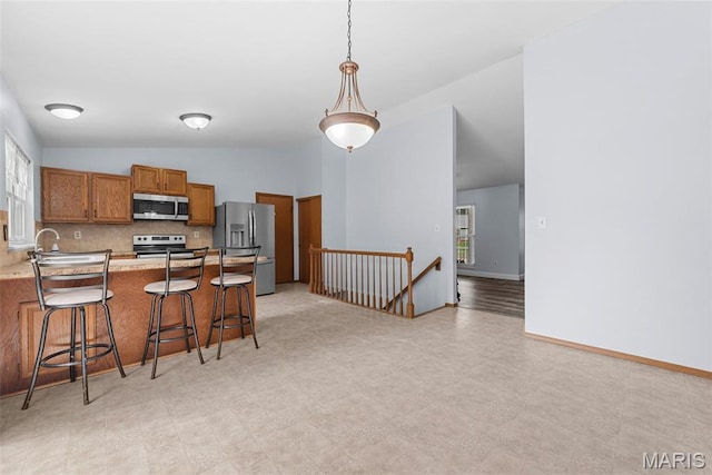 1203 Summerwood Dr, Saint Peters, MO 63376 - kitchen featuring stainless steel appliances, vaulted ceiling, brown cabinetry, decorative backsplash, and a kitchen breakfast bar