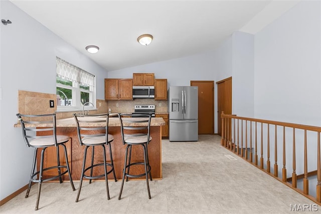 1203 Summerwood Dr, Saint Peters, MO 63376 - kitchen featuring appliances with stainless steel finishes, a peninsula, brown cabinets, backsplash, and vaulted ceiling