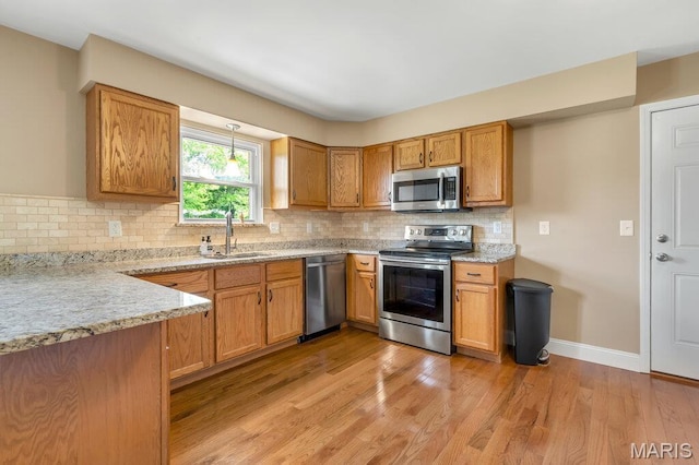3100 Tally Ho Dr, Saint Charles, MO 63301 - kitchen with appliances with stainless steel finishes, light wood-style flooring, decorative backsplash, brown cabinetry, and light stone countertops