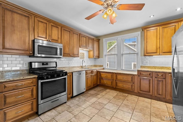542 S Main St, Waterloo, IL 62298 - kitchen with stainless steel appliances, brown cabinetry, tasteful backsplash, ceiling fan, and light stone countertops