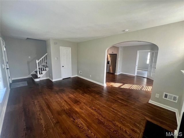 2328 Rockdale Ave, Saint Louis, MO 63121 - unfurnished living room featuring arched walkways, dark wood-type flooring, baseboards, and stairway