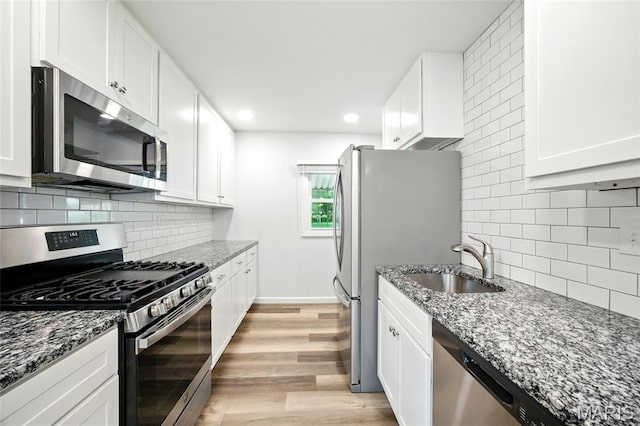 7825 Delmont St, Saint Louis, MO 63123 - kitchen featuring stainless steel appliances, a sink, white cabinetry, dark stone counters, and light wood-style floors