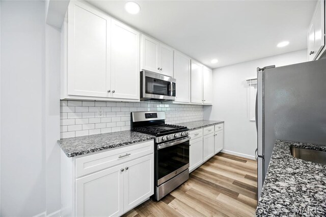 7825 Delmont St, Saint Louis, MO 63123 - kitchen with stainless steel appliances, white cabinets, light wood-type flooring, dark stone countertops, and tasteful backsplash