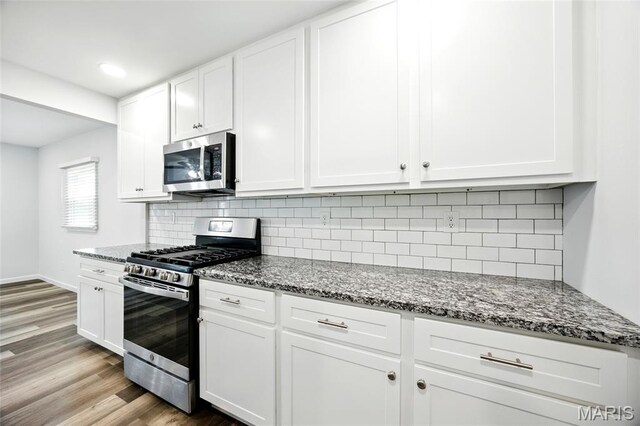 7825 Delmont St, Saint Louis, MO 63123 - kitchen featuring appliances with stainless steel finishes, dark stone countertops, white cabinetry, backsplash, and recessed lighting
