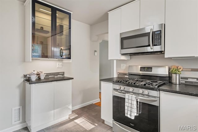 657 Lilac Ave, Webster Groves, MO 63119 - kitchen featuring stainless steel appliances, dark countertops, white cabinets, light tile patterned floors, and glass insert cabinets