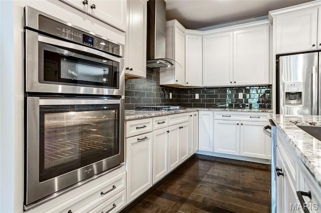 2216 Cournier St, Saint Charles, MO 63301 - kitchen with appliances with stainless steel finishes, wall chimney exhaust hood, white cabinetry, backsplash, and dark wood-style flooring