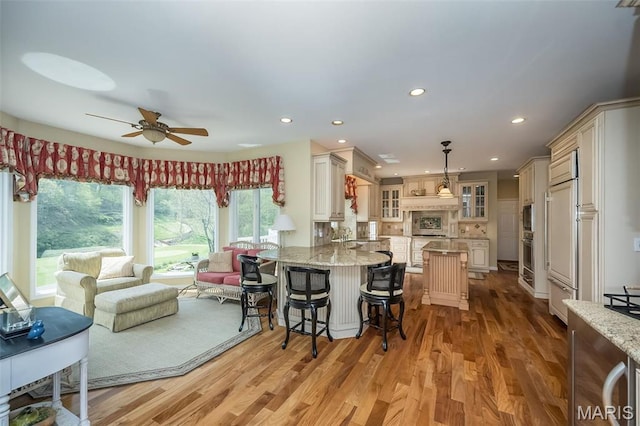 1417 Wheatfield Ln, Saint Albans, MO 63073 - kitchen featuring glass insert cabinets, light stone counters, ceiling fan, a breakfast bar area, and recessed lighting