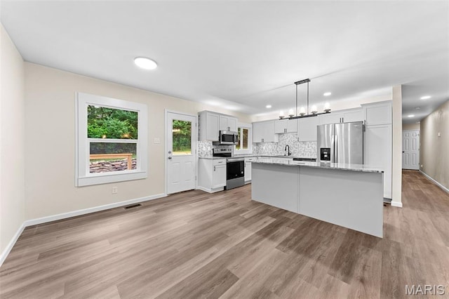 2019 San Pedro Dr, Arnold, MO 63010 - kitchen with appliances with stainless steel finishes, light wood finished floors, tasteful backsplash, a center island, and pendant lighting