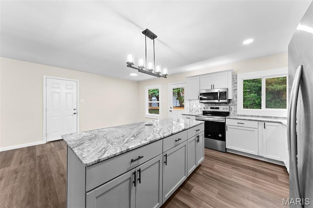2019 San Pedro Dr, Arnold, MO 63010 - kitchen featuring stainless steel appliances, a center island, decorative backsplash, dark wood-style floors, and light stone counters
