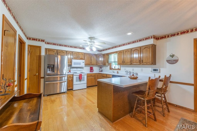 39 Rock Ridge Rd, Wappapello, MO 63966 - kitchen with white appliances, a textured ceiling, a peninsula, light wood-type flooring, and brown cabinetry