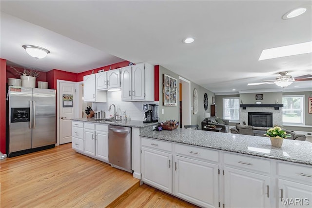 923 N Geyer Rd, Kirkwood, MO 63122 - kitchen with appliances with stainless steel finishes, a fireplace, a skylight, light wood-style floors, and white cabinets