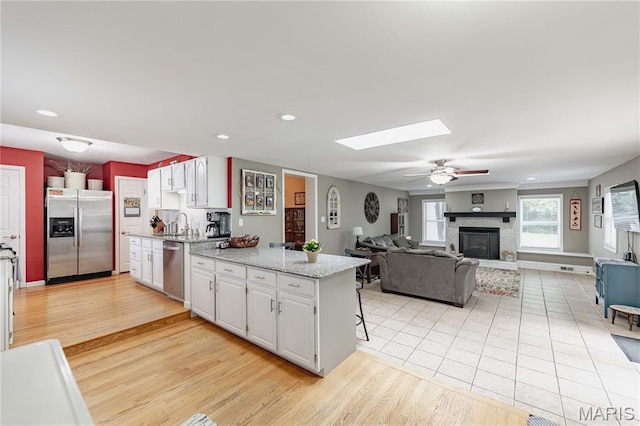 923 N Geyer Rd, Kirkwood, MO 63122 - kitchen featuring stainless steel appliances, a glass covered fireplace, white cabinets, a skylight, and a ceiling fan