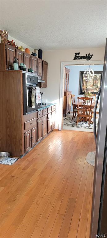 405 E Bittersweet Dr, Gerald, MO 63037 - kitchen with black oven, freestanding refrigerator, a textured ceiling, and light wood-type flooring