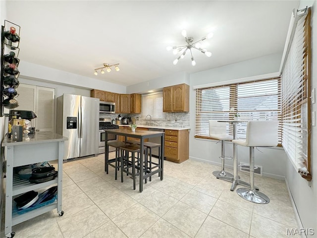 1001 Pike St, Saint Charles, MO 63301 - kitchen with appliances with stainless steel finishes, tasteful backsplash, light tile patterned flooring, brown cabinetry, and a chandelier