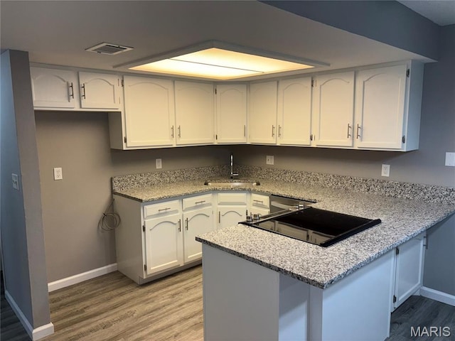 1420 Heritage Lndg Unit 107, Saint Charles, MO 63303 - kitchen with a peninsula, light wood finished floors, white cabinetry, and light stone counters