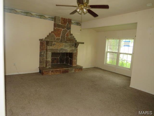 705 S Arch St, Jerseyville, IL 62052 - unfurnished living room featuring ceiling fan, carpet flooring, and a stone fireplace