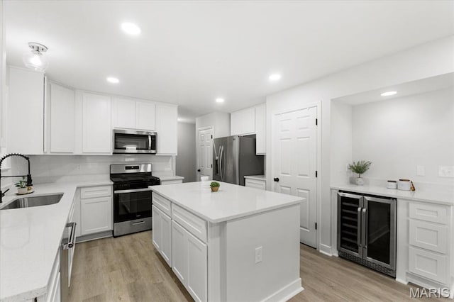 4507 Behlmann Grove Pl, Florissant, MO 63034 - kitchen with wine cooler, stainless steel appliances, a center island, light wood-style flooring, and white cabinets