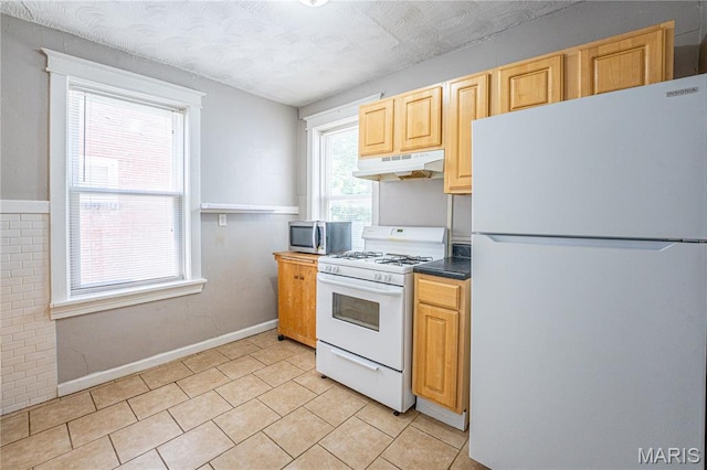 1323 Woodland Dr, Saint Louis, MO 63117 - kitchen featuring white appliances, under cabinet range hood, dark countertops, light tile patterned floors, and light brown cabinetry