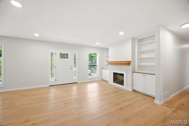 6905 Scenic View Dr, Cedar Hill, MO 63016 - unfurnished living room featuring built in shelves, healthy amount of natural light, light wood-style floors, a glass covered fireplace, and recessed lighting