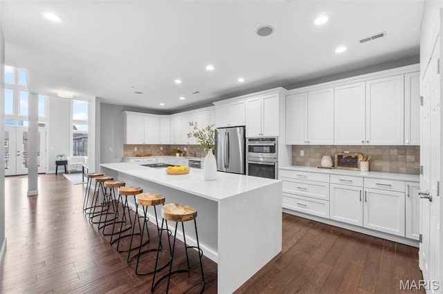 110 N Newstead Ave Unit 303, Saint Louis, MO 63108 - kitchen with appliances with stainless steel finishes, light countertops, white cabinetry, dark wood-style flooring, and decorative backsplash