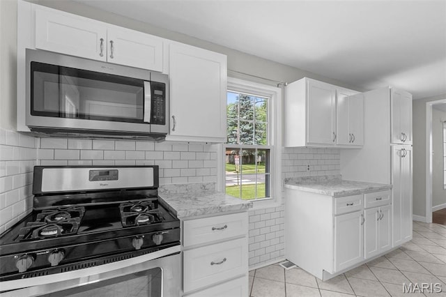 2490 Mullanphy Ln, Florissant, MO 63031 - kitchen featuring stainless steel appliances, white cabinets, light tile patterned floors, and decorative backsplash