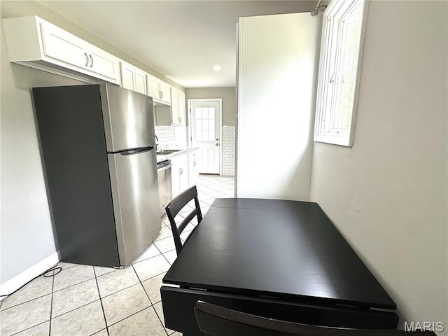 2490 Mullanphy Ln, Florissant, MO 63031 - kitchen featuring freestanding refrigerator, light tile patterned floors, white cabinets, decorative backsplash, and light countertops