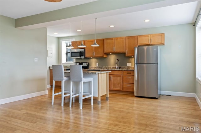 4220 Mcpherson Ave Unit 303, Saint Louis, MO 63108 - kitchen featuring appliances with stainless steel finishes, a kitchen breakfast bar, a center island, light wood-type flooring, and hanging light fixtures