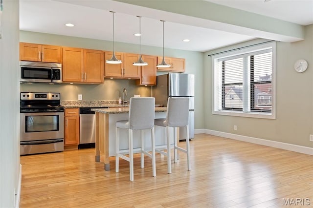 4220 Mcpherson Ave Unit 303, Saint Louis, MO 63108 - kitchen with stainless steel appliances, a kitchen bar, light wood-style flooring, a center island, and decorative light fixtures