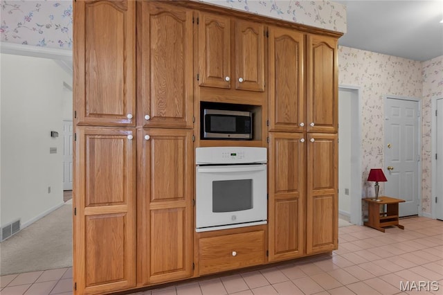 2615 Saddle Ridge Ln, Cape Girardeau, MO 63701 - kitchen featuring oven, wallpapered walls, stainless steel microwave, light tile patterned flooring, and brown cabinetry